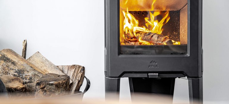 Jøtul F 163 black wood stove with logs on the side and  white wall at the back 